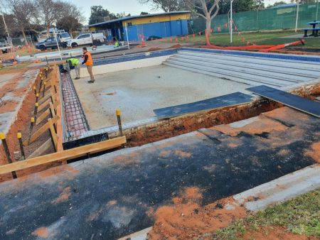 photograph showing the excavation around the middle-sized childrens pool, filled with boarding and rebar ready for concreting. Two workers in high vis vests stand in the pool.