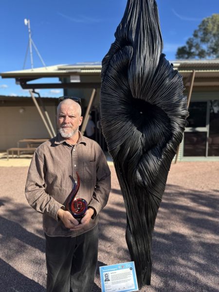2026 Solar and Sun Grand Prize Winner Hugh Avey posing next to his winning sculpture 